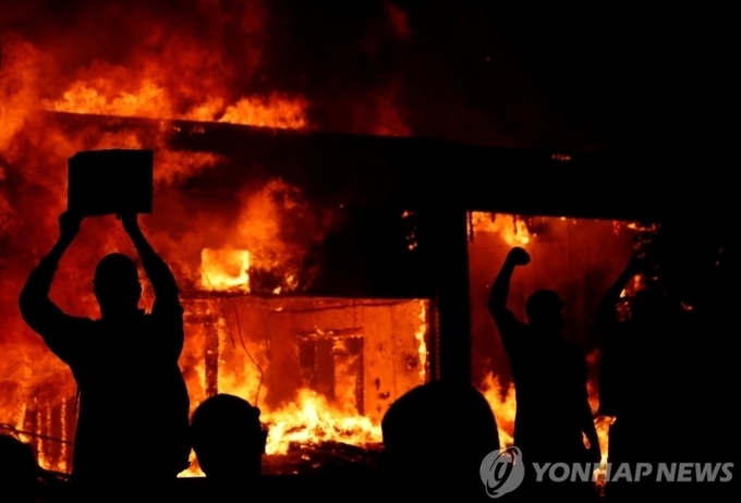  30일(현지시간) 미국 미니애폴리스에서 비무장 흑인 조지 플로이드가 백인 경찰의 가혹 행위로 숨진 사건에 항의하는 시위대,. 방화로 불타는 건물에 환호하고 있다. 미니애폴리스 로이터=연합뉴스)