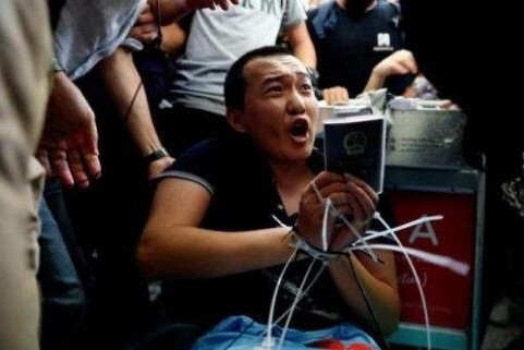 시위대에 의해 공항카트에 손발이 묶인 채, 자신의 신분증과 여권을 들어 보이며 환구시보 기자라고 항의하는 푸 꾸어 하오 기자의 모습.